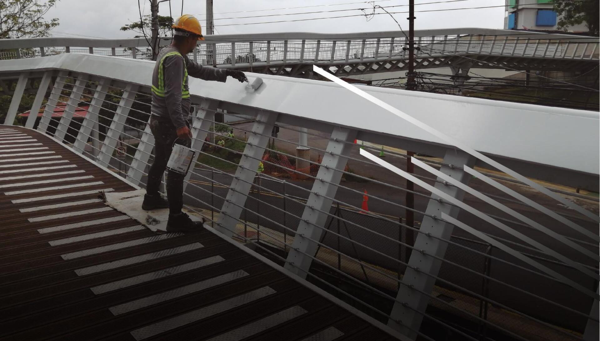Pintor de Prisma Arquitectos aplicando acabado en estructura metálica de un puente peatonal en Costa Rica
